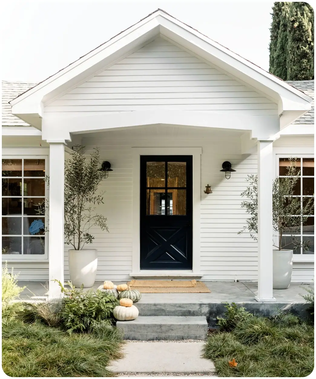 White house entrance with pumpkins and plants.